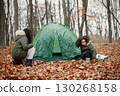 Beautiful little black girls in tent camping in the forest. Two little sisters are puting up a tent in autumn forest. Black girls wearing khaki coats. 130268158