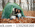 Beautiful little black girls in tent camping in the forest. Two little sisters sitting in a tent in autumn forest and looking on a globe. Black girls wearing khaki coats. 130268160