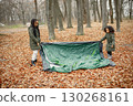 Beautiful little black girls in tent camping in the forest. Two little sisters are puting up a tent in autumn forest. Black girls wearing khaki coats. 130268161