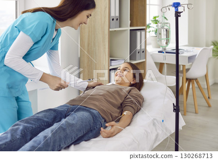 Teenage child girl lying on couch in clinic while receiving IV drip infusion and vitamin therapy. Teenage child girl lying on couch in clinic while receiving IV drip infusion and vitamin therapy. 130268713