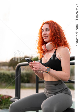 Redhead female jogger using smartphone at gym park 130269473