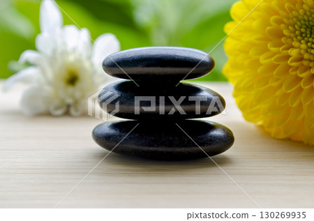 Elegant zen stones with vibrant yellow flower on wooden background with customizable space for text 130269935