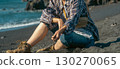A girl in casual clothes sits on a black volcanic beach by the Atlantic ocean. 130270065