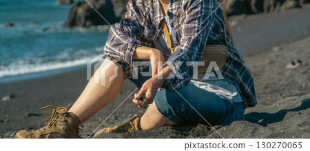 A girl in casual clothes sits on a black volcanic beach by the Atlantic ocean. A girl in casual clothes sits on a black volcanic beach by the Atlantic ocean. 130270065