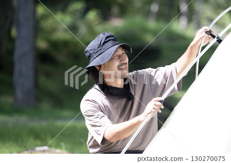 A person setting up a tent at a campsite in a beautiful green forest 130270075