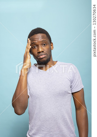 Portrait of an upset male adult experiencing a migraine, pressing his temple to relieve discomfort. Unwell african american man feeling the strain of a headache, looking for relief. Portrait of an upset male adult experiencing a migraine, pressing his temple to relieve discomfort. Unwell african american man feeling the strain of a headache, looking for relief. 130270634