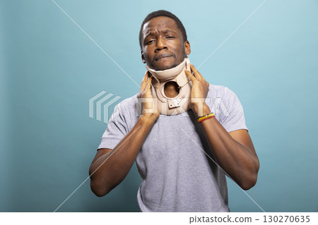 Injured adult using a neck brace to heal from a vertebra fracture, showing signs of physical discomfort. Hurt black man with cervical collar recovering from a fractured vertebra, visibly in pain. 130270635