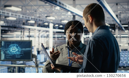 Data center coworkers doing brainstorming, monitoring deep learning processes, reviewing operational metrics. Colleagues working together to review neural networks reports during inspection, camera B Data center coworkers doing brainstorming, monitoring deep learning processes, reviewing operational metrics. Colleagues working together to review neural networks reports during inspection, camera B 130270656