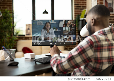 Black remote worker drinking coffee and listening to diverse colleagues during virtual meeting. African american entrepreneur in online brainstorming session, sharing strategic business ideas with Black remote worker drinking coffee and listening to diverse colleagues during virtual meeting. African american entrepreneur in online brainstorming session, sharing strategic business ideas with 130270744