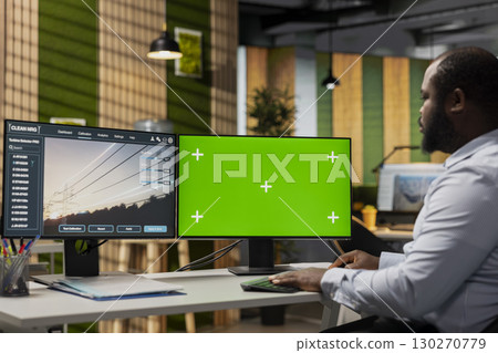 Engineer using green screen PC to refine transmission tower systems, improving renewable energy integration. RD expert uses mockup computer in office to design eco power lines infrastructure 130270779