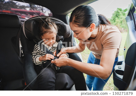 mother is fastening safety belt to toddler girl in car seat, safety baby chair travelling mother is fastening safety belt to toddler girl in car seat, safety baby chair travelling 130271879