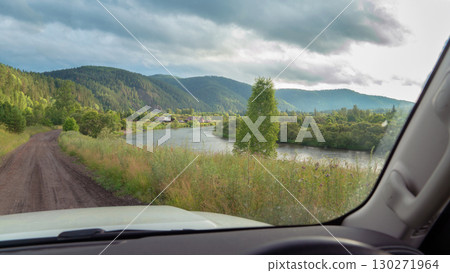 Scenic drive along riverside landscape with mountains in background during cloudy afternoon. Road trip to remote villages in Siberia and Russia river view Scenic drive along riverside landscape with mountains in background during cloudy afternoon. Road trip to remote villages in Siberia and Russia river view 130271964
