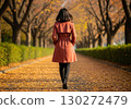 Back view of a woman wearing a beige coat walking on a carpet of fallen leaves 130272479