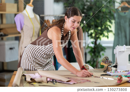 Female fashion designer drawing on paper with curved rulers in workshop 130273808
