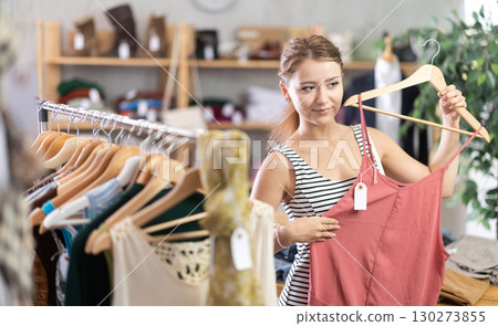 Young woman chooses a set of clothes for the summer. Visitor to the boutique examines new summer collection of clothes Young woman chooses a set of clothes for the summer. Visitor to the boutique examines new summer collection of clothes 130273855