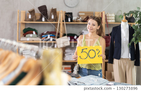 Portrait of young girl holding sign saying 50 percent discount in clothing store Portrait of young girl holding sign saying 50 percent discount in clothing store 130273896