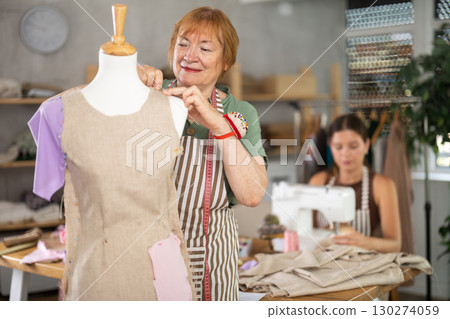 Elderly woman working with mannequin, young woman sewing Elderly woman working with mannequin, young woman sewing 130274059