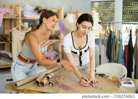 Two female dressmakers sketching garment patterns with curve ruler in sewing studio Two female dressmakers sketching garment patterns with curve ruler in sewing studio 130274061