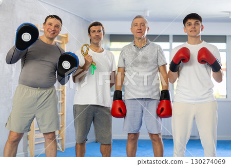Four men of different ages in gym at group training session looking straight with sports equipment 130274069