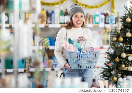 Young woman buyer with filled basket household chemistry wanders around store 130274107