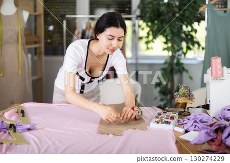 Female clothing designer securing pattern to fabric on worktable Female clothing designer securing pattern to fabric on worktable 130274229