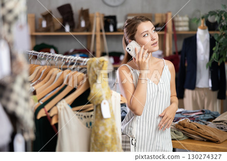 Young woman consults on her mobile phone about which jeans to choose in clothing store 130274327