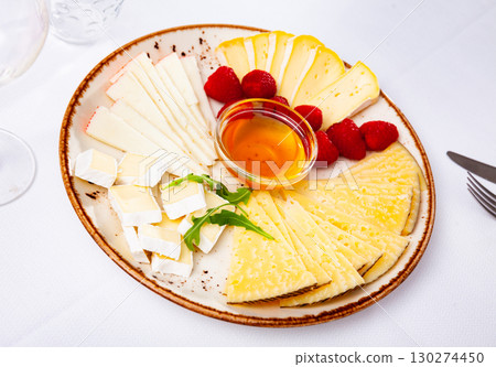 Slices of hard and soft cheeses on plate with raspberries and honey 130274450