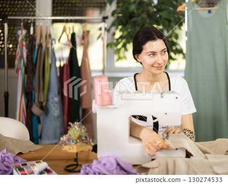 Female clothing designer stitching fabric on sewing machine in studio Female clothing designer stitching fabric on sewing machine in studio 130274533