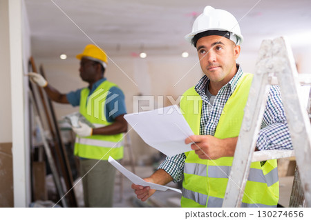 Man builder examining project documentation in apartment Man builder examining project documentation in apartment 130274656