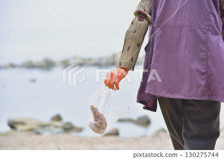 Rear view of a senior woman picking up shells on the beach 130275744