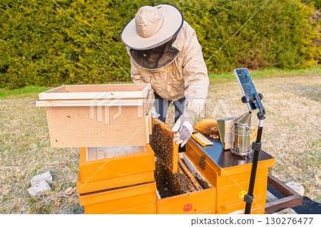 Beekeeper Inspecting Honeycomb Frame and Recording Video for Online Bee Keeping Course 130276477
