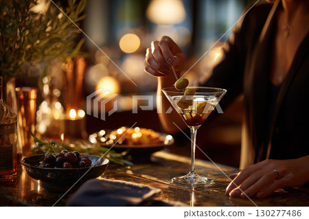 Bartender adds olive to a classic martini at a stylish bar 130277486