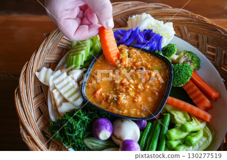 A hand is dipping Chili paste with fresh vegetables, asain cuisine A hand is dipping Chili paste with fresh vegetables, asain cuisine 130277519
