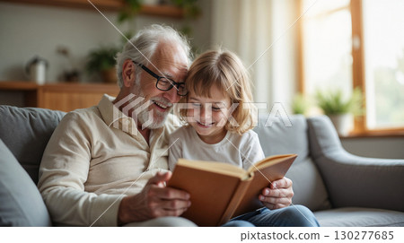 Grandfather reading a book to his grandchild in a bright living room, both smiling. 130277685