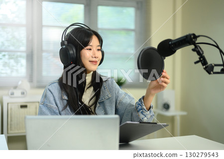 Young woman wearing headphones adjusting microphone while recording podcast at home studio Young woman wearing headphones adjusting microphone while recording podcast at home studio 130279543