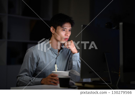 Office worker eating instant noodles while working overtime in dimly lit office 130279566