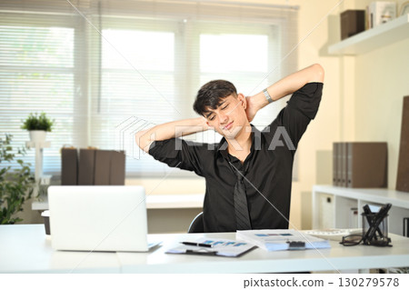 Tired businessman stretching his neck at desk after long hours of computer work in modern office. Tired businessman stretching his neck at desk after long hours of computer work in modern office. 130279578