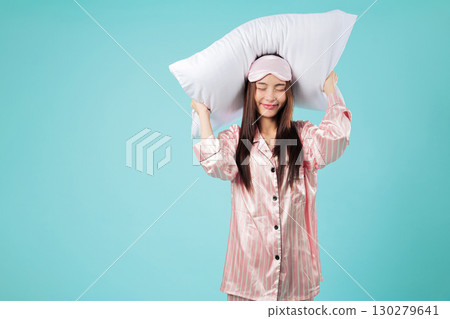 Young Asian woman ready for sleep, dream of a restful night, pillow over head, wearing pajamas and smiling, she is enjoying this good sleep, resting well, headshots isolated studio blue background 130279641