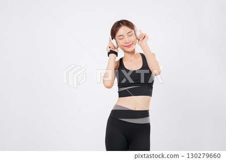 Dance with joy as a fit Asian woman enjoys her favorite music in headphones. Her energy flows as she starts to dance again, expressing freedom and happiness in her lifestyle. isolated white background 130279660