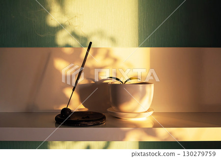 Incense stick burning on shelf with smoke. Plant in small pot. Spiritual aromatherapy and meditation concept. 130279759