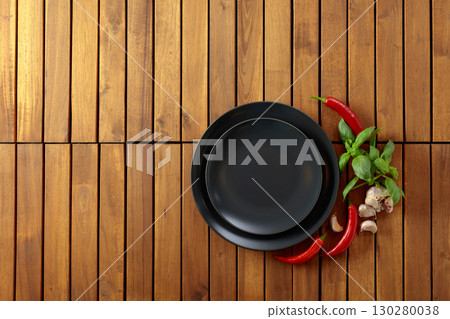 Empty black plate, garlic, basil, and red pepper on a natural wooden background. 130280038