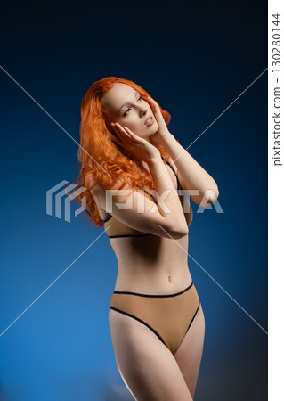Woman with flowing red hair poses gracefully in a colorful light setting Woman with flowing red hair poses gracefully in a colorful light setting 130280144