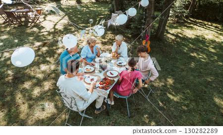 Aerial shot of family gathering for barbecue in summer garden, talking and eating grilled food. Aerial shot of family gathering for barbecue in summer garden, talking and eating grilled food. 130282289