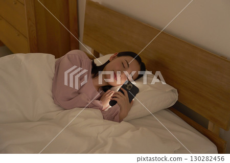 一名女子在床上玩智慧型手機時睡著了 130282456