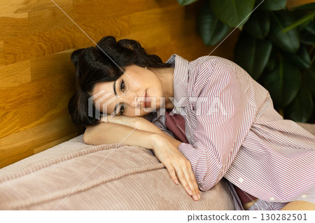Depressed woman with hair rollers sitting on sofa and thinkiing. 130282501