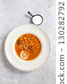 Rich soup with smoked meats, sausages, lemon, and olives, viewed from above on a gray background 130282792