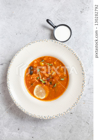 Rich soup with smoked meats, sausages, lemon, and olives, viewed from above on a gray background Rich soup with smoked meats, sausages, lemon, and olives, viewed from above on a gray background 130282792