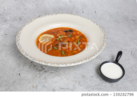 Rich soup with smoked meats, sausages, lemon, and olives on a gray background 130282796