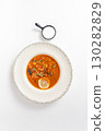 Rich soup with smoked meats, sausages, lemon, and olives, viewed from above on a white background 130282829