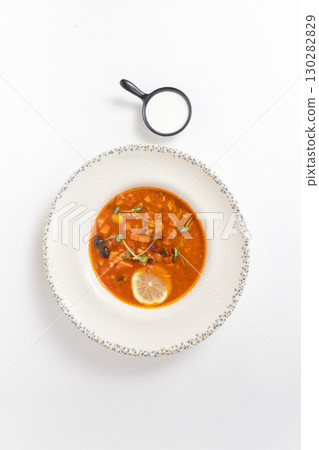 Rich soup with smoked meats, sausages, lemon, and olives, viewed from above on a white background 130282829